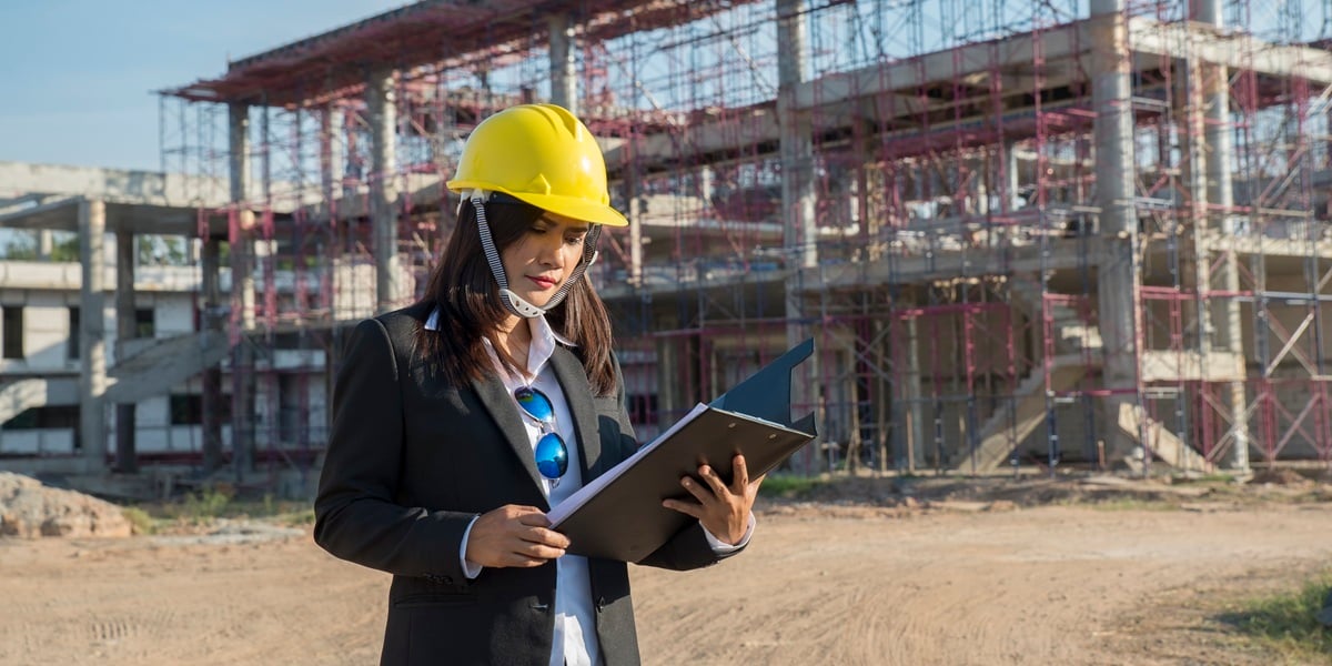 Commercial construction manager in a hard hat reviewing plans at a commercial construction site