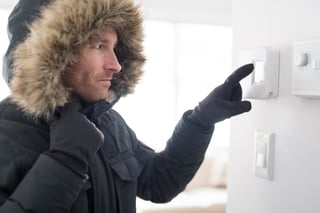 man in parka adjusting thermostat inside his home
