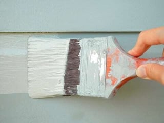 woman touching up paint on house