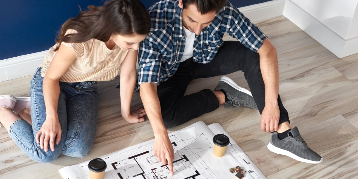A couple sitting on the ground looking at floorplan.